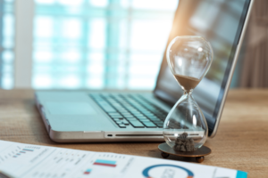 Hour Glass half full next to a laptop