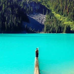 Person standing on a small pier surrounded by glacier water looking at the mountains